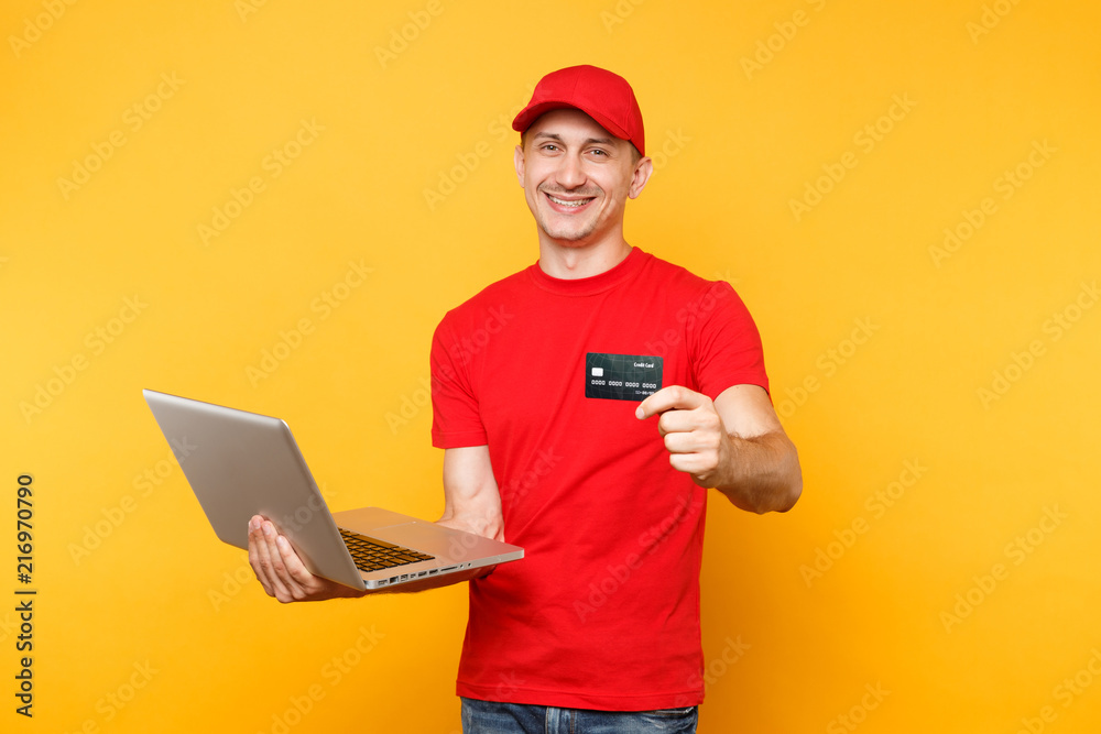 Delivery man isolated on yellow orange background. Professional male employee courier in red cap, t-shirt holding laptop pc computer, credit bank card. Service concept. Copy space for advertisement. Delivery man isolated on yellow orange background. Professional male employee courier in red cap, t-shirt holding laptop pc computer, credit bank card. Service concept. Copy space for advertisement.
