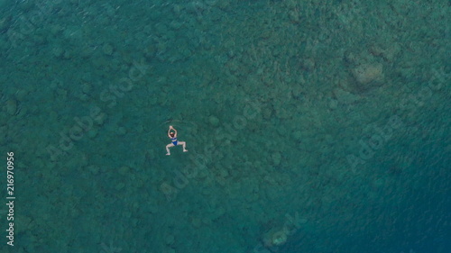 AERIAL: woman floating on blue water surface, swimming in transparent mediterranean sea, top down view, summer vacation concept