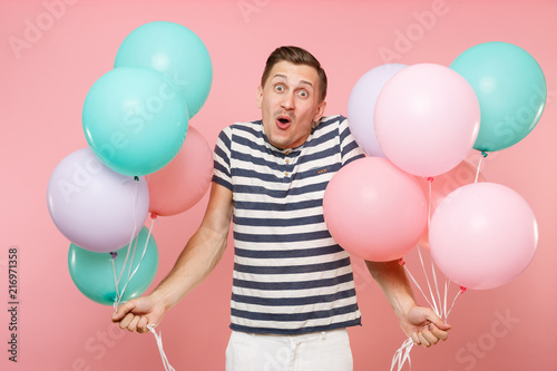 Portrait of fascinating young happy man wearing striped t-shirt holding colorful air balloons isolated on bright trending pink background. People sincere emotions lifestyle concept. Advertising area. © ViDi Studio