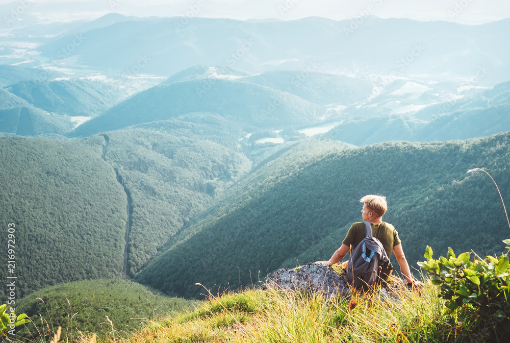 Young man tourist sits on top on hill with beautiful valley panorama