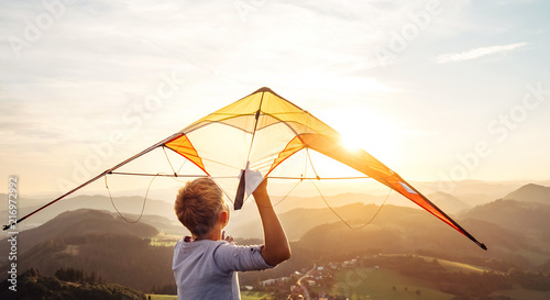 Boy starts to fly a kite over the mountain hills at sunset time photo