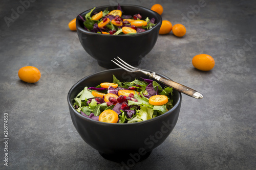 Bowl of mixed green salad with red cabbage, kumquat and pomegranate seeds