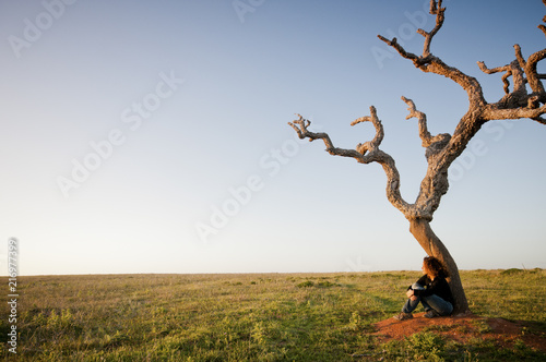 lonely young caucasian woman sitting on a dead tree base and looking at the horizon. freedom and relaxing concept for people that enjoy the outdoor nature. travel and live different.