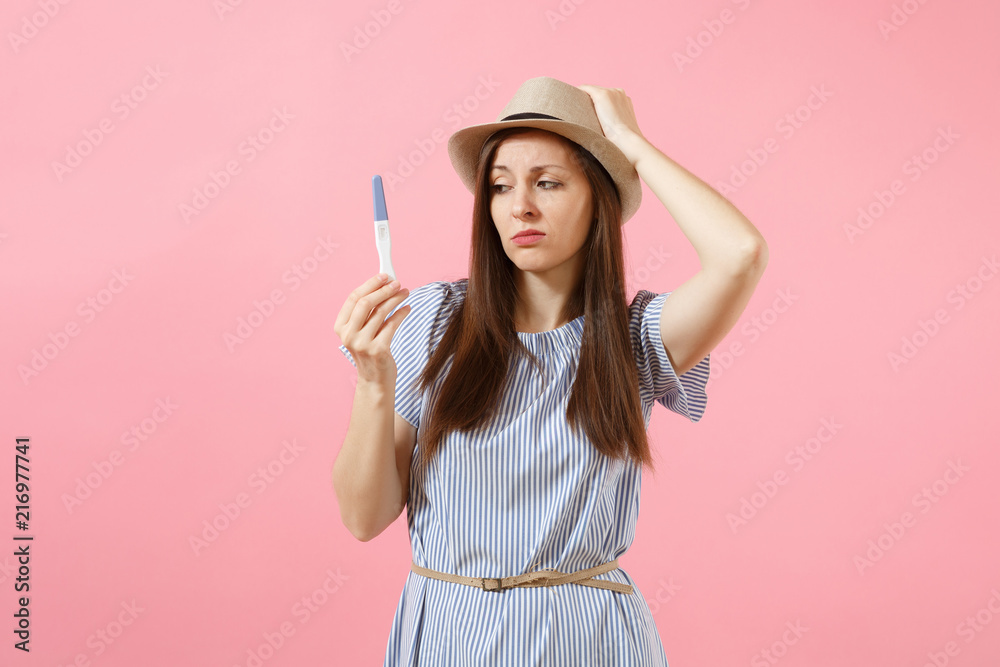 Sad unhappy woman in blue dress, hat hold in hand, looking at pregnancy test isolated on pink background. Medical healthcare gynecological, pregnancy fertility maternity people concept. Copy space.