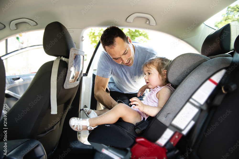 father putting his child daughter into her car seat in the car father putting his child daughter into her car seat in the car