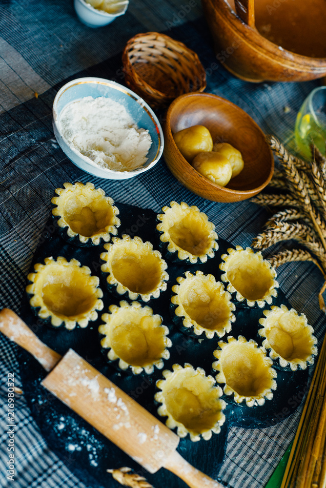 Still life in country style. Close up tartlets in baking dishes before bake with spikelets and rolling pin on black stone stand. Top view
Still life in country style. Close up tartlets in baking dishes before bake with spikelets and rolling pin on black stone stand. Top view