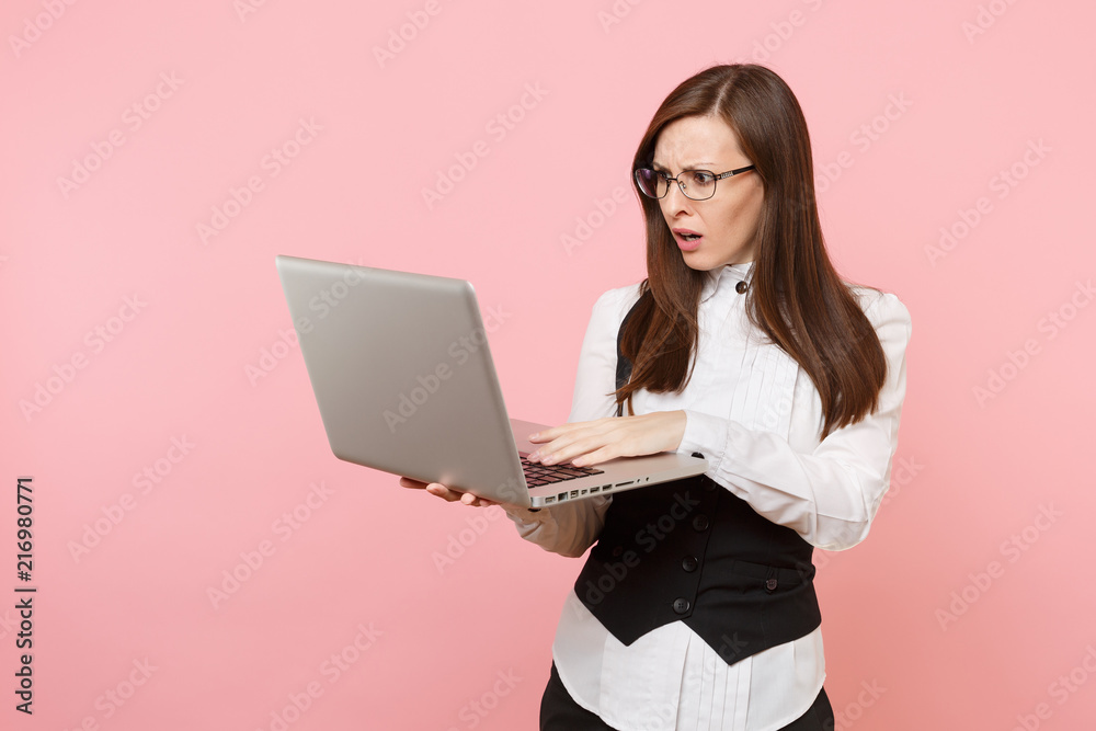 Young shocked concerned business woman in suit and glasses working in laptop pc computer isolated on pastel pink background. Lady boss. Achievement career wealth concept. Copy space for advertisement. Young shocked concerned business woman in suit and glasses working in laptop pc computer isolated on pastel pink background. Lady boss. Achievement career wealth concept. Copy space for advertisement.