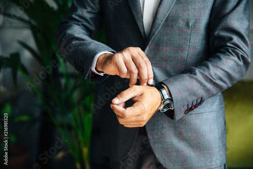 Close-up of a cropped frame of a man in a business suit buttoning his expensive watch on his hand. A businessman is going to work, putting on a leather watch. A bridegroom is going to a wedding.