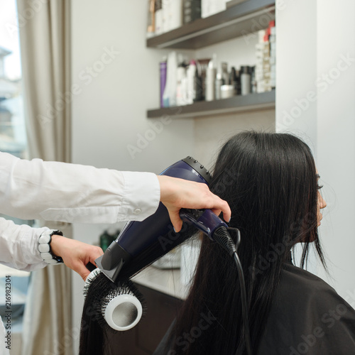 Professional stylist drying brunette woman's hair in salon