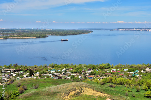 view of the bend of the Volga River from the hill, suburban and urban buildings, coastline, islands, green vegetation, tanker going along the river in the background, Saratov, Russia