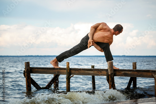 Young yoga trainer practicing parivrita Parswakonasana pose on a wooden pier on a sea or river shore photo