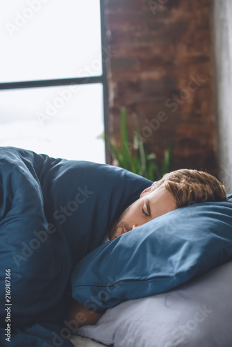 close up view of young handsome man sleeping under blanket in his bed at home