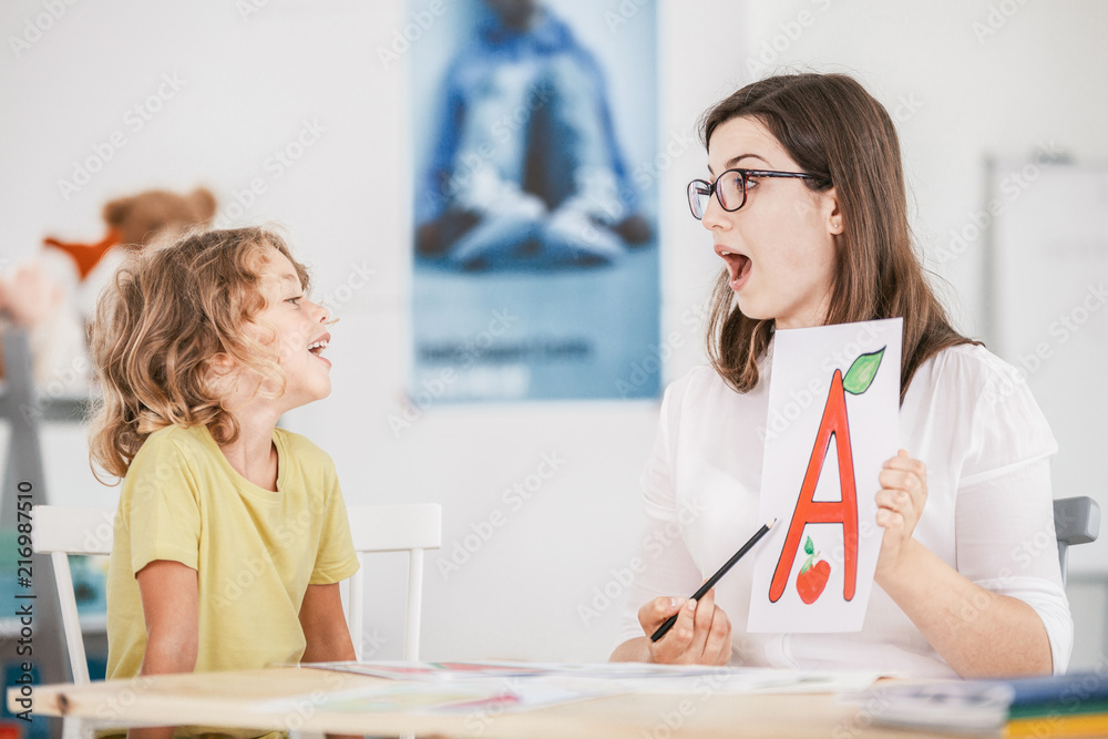 Speech therapist working with a child on a correct pronunciation using a prop with a letter 'a' picture. - obrazy, fototapety, plakaty 
