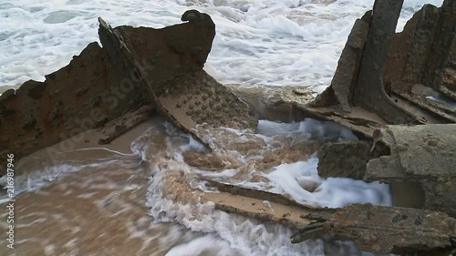 Close up of a ship wrecks hull on the beach surrounded by calm waves photo