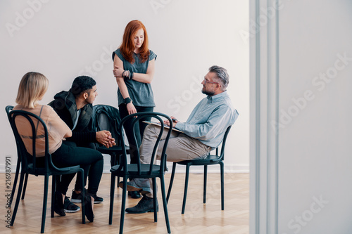 Shy rebellious girl talking about problem with psychotherapist during group therapy