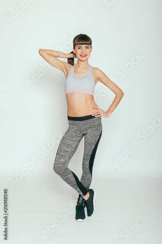 health, people, Sport and lifestyle concept - Young happy fitness girl with sporty body at studio on a gray background. Beautiful fit Girl. Fitness model in gray sportswear. Healthy lifestyle.