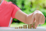 Woman hand putting coin, gold coins stack on wooden table in the morning sunlight. business, investment, retirement, finance and Money Saving for the future concepts