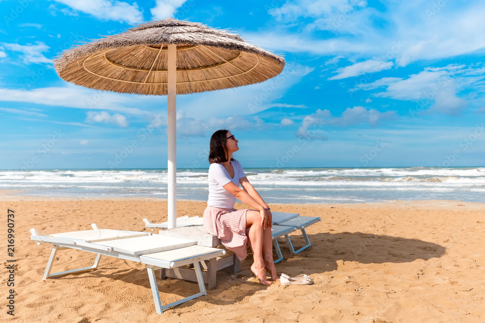 Girl sitting under sun umbrella on seashore. Rimini beach, Italy.