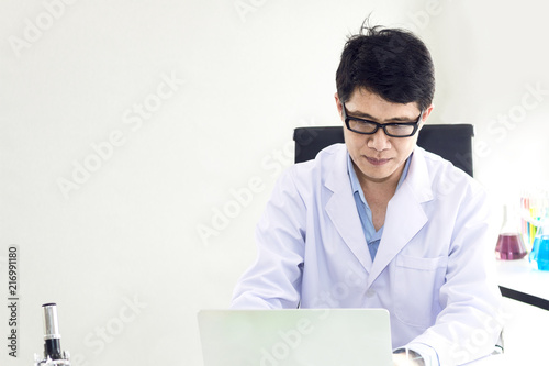 Portrait of a smiling mature scientist in a white coat with glass near laptop at the white science laboratory.Copy space