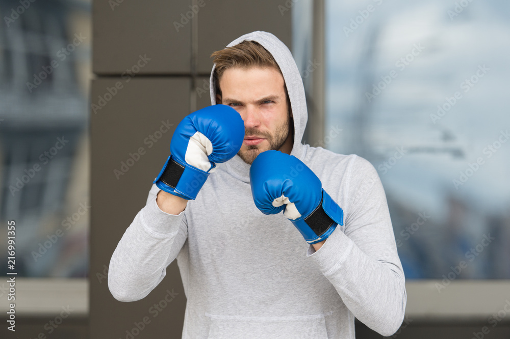 Strong and full of energy. Sportsman concentrated training boxing gloves. Athlete concentrated face with sport gloves practice fighting skills urban background. Boxer handsome strict coach practicing