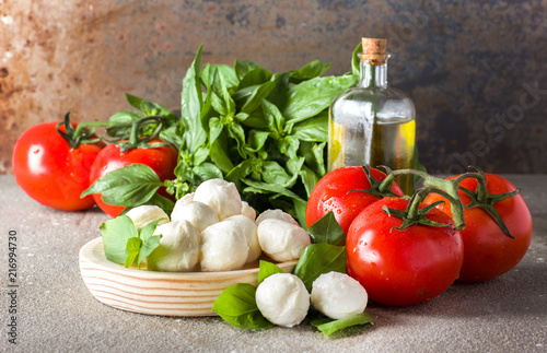 Balls of mozzarella with basil leaves, tomato and olive oil on rustic background