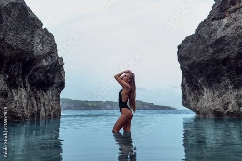 Beautiful girl in a black swimsuit in a blue lagoon among the rocks
 photo