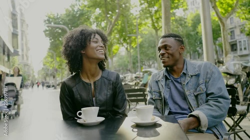 Young happy black couple drinking coffee in street cafe