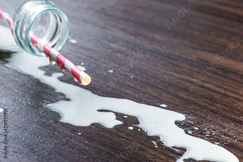 Fotografia split milk from a bottle on wooden table, close-up milk droplet on tip of straw