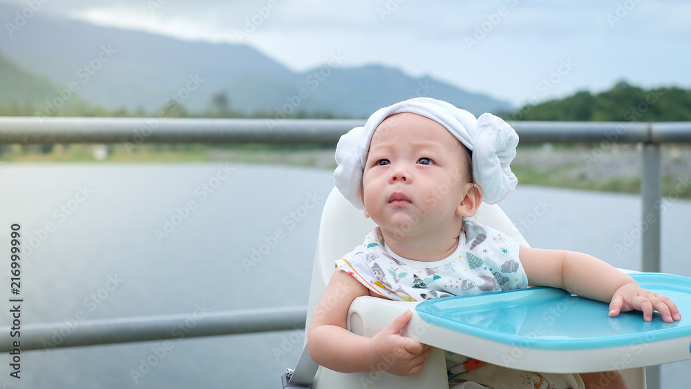 Φωτογραφία The Asian little baby sit on the chair on the big rock near the dam