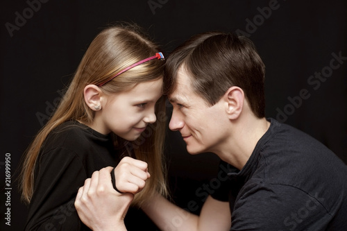 Daughter with dad is having fun on a black background. The father holds the hand for his daughter who as if wants to bit him