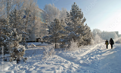 The street of the town in winter, snowy trees, a woman and a child are walking along the snowy path.