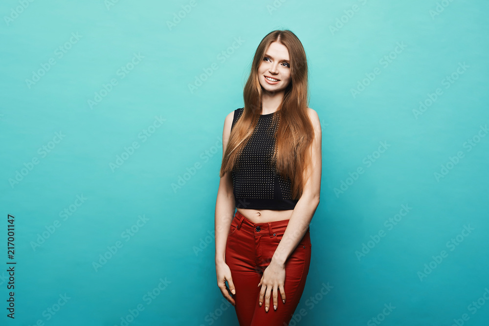 Fashionable and beautiful blonde model girl with perfect body in black stylish t-shirt and in trendy red pants posing at blue background at sudio, isolated Fashionable and beautiful blonde model girl with perfect body in black stylish t-shirt and in trendy red pants posing at blue background at sudio, isolated