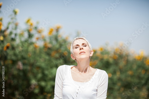 Beautiful middle age woman in a rural field scene outdoors with sunflowers, enjoying sunlight, summerly, autumn mood 