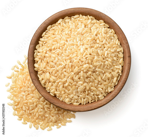 raw brown rice in the wooden plate, isolated on the white background, top view