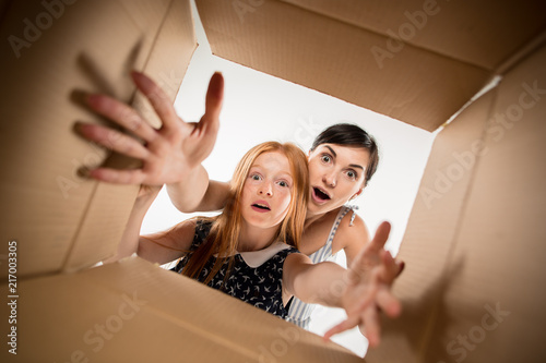 The surprised mom and daughter unpacking, opening carton box and looking inside. The package, delivery, surprise, gift lifestyle concept. Human emotions and facial expressions concepts