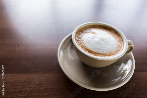 Cappuccino coffee cup on wooden table near windows