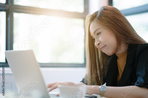 Young woman sitting in coffee shop at wooden table, drinking coffee and using laptop.On table is laptop. Girl browsing internet, chatting, blogging. Female holding laptop and looking on his screen.