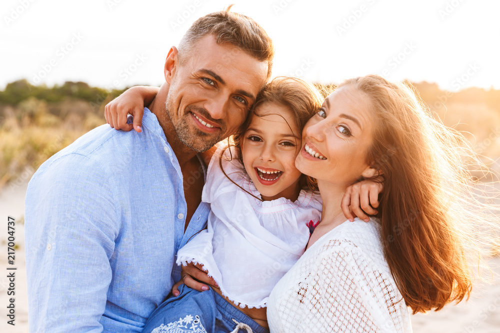 Fototapeta premium Parents having fun together outdoors at the beach with their daughter.
