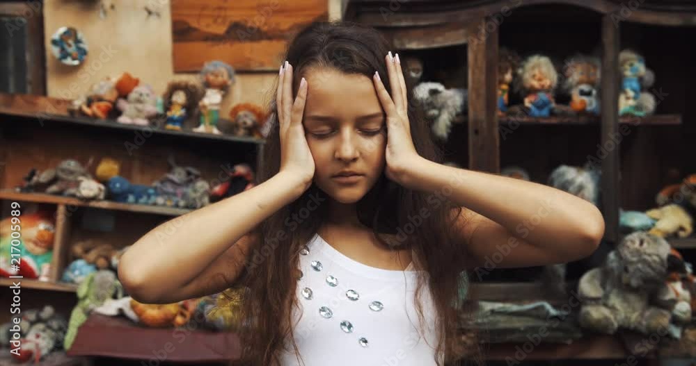 Portrait of the 10 years old girl. Strange kid is touching her head and deeply looking at camera. garden full of toys and old furniture location. 4k.