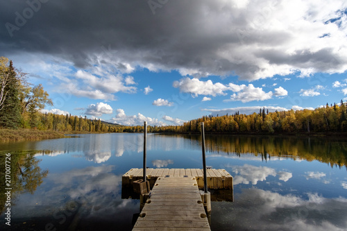 Pier on the Talkeetna lakes, open lake, autumn trees and reflection of clouds.