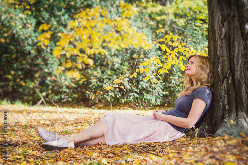 young blond hair woman sit under tree in autumn forest and dreaming 