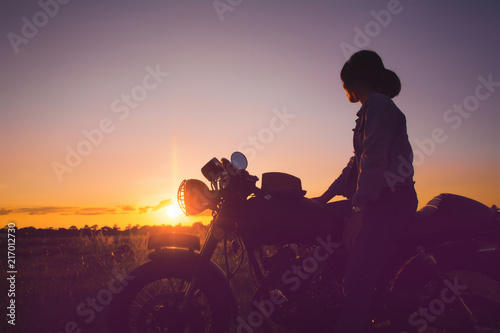Silhouette of young woman drive with motorcycle on street, enjoying freedom and active lifestyle, having fun on a bikers tour on sunset background.