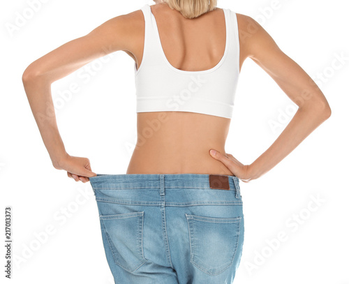 Young slim woman in old big jeans showing her diet results on white background © New Africa