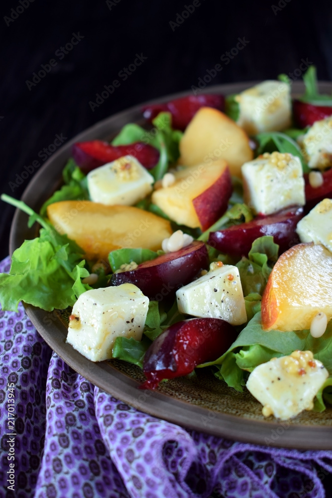 Fruit salad with arugula, plums, nectarines and soft cheese on a plate