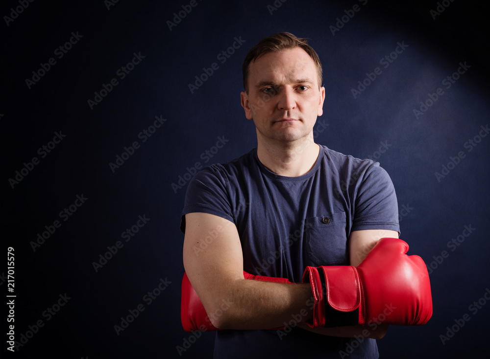 Middle aged man posing crossed his hands with boxing gloves on a dark background