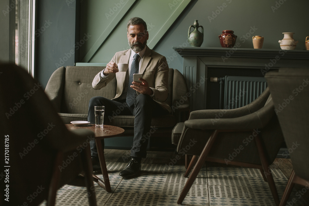 Handsome senior businessman drinking coffee and using mobile phone in lobby Handsome senior businessman drinking coffee and using mobile phone in lobby