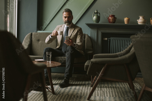 Handsome senior businessman drinking coffee and using mobile phone in lobby © BGStock72