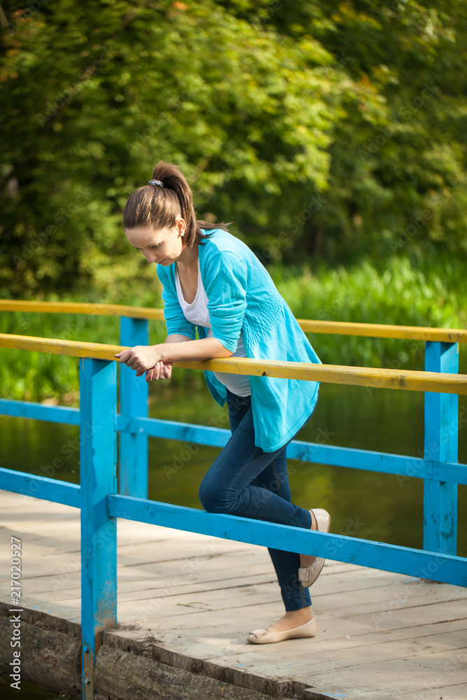 Portrait of a young happy pregnant woman on a blue wooden bridge.