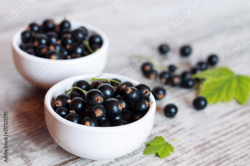 Black currant in two small bowls on a white wooden table.
