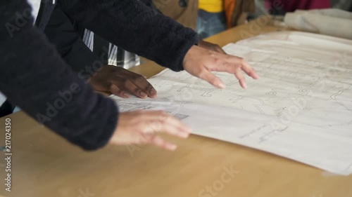 Three young people discuss the plans for a building project in a work area. They gesture with their hands as they discuss. photo